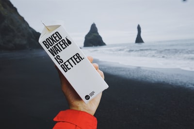 冰岛海滩前，一个人拿着一盒装水的纸箱